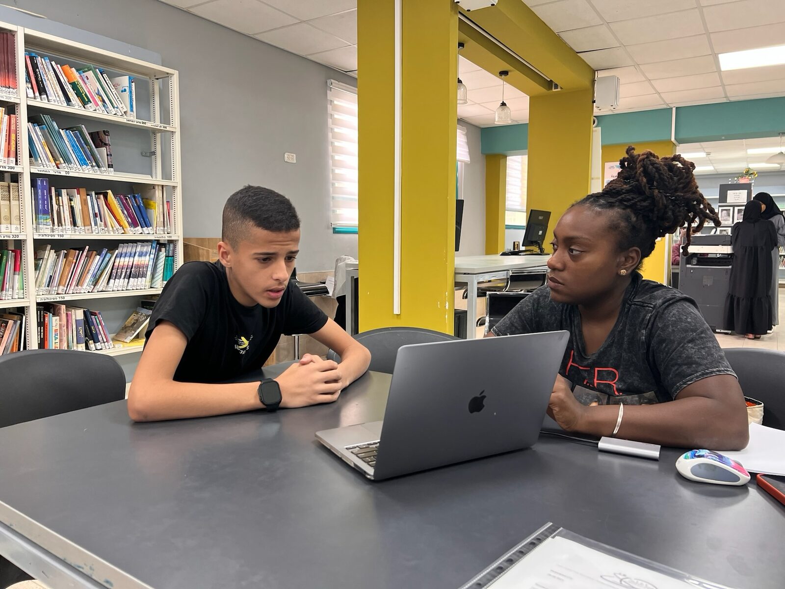 A teacher helping a student one-on-one at a laptop in the school library