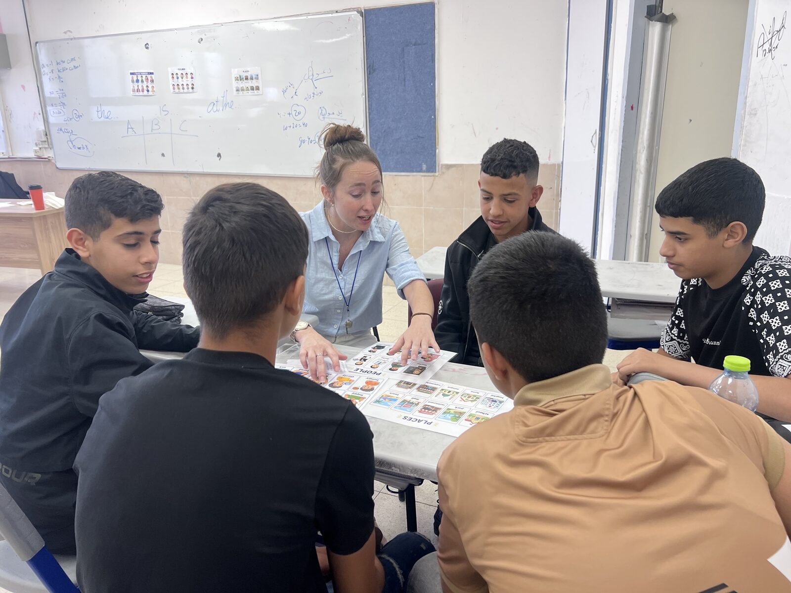 A teacher and students around a table playing a picture-card vocabulary game