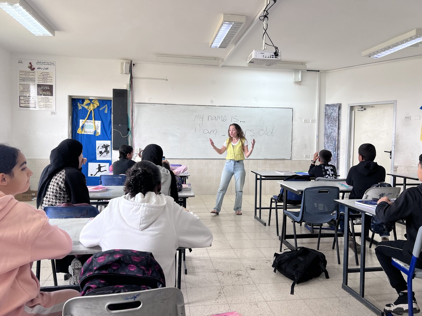 A teacher leading an English lesson at the whiteboard as students follow along
