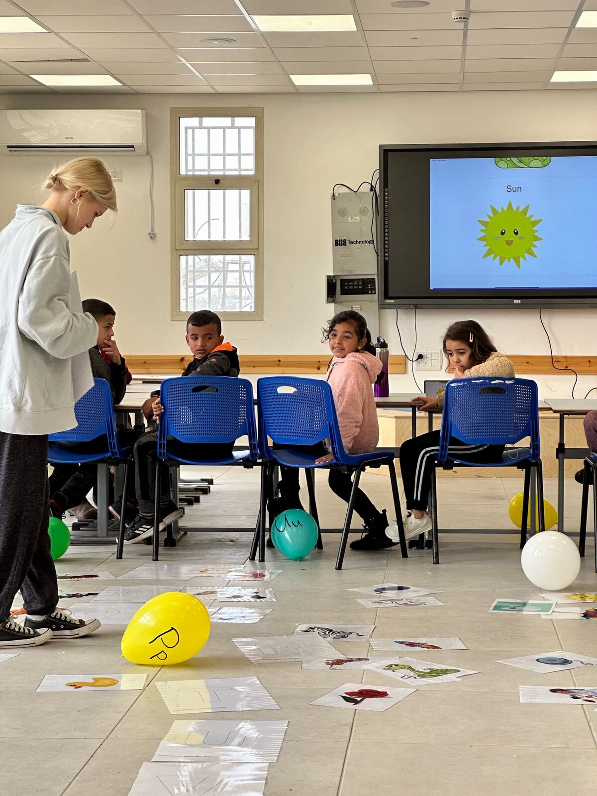 A teacher leading young students in an active floor game with balloons and letter cards
